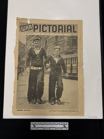 A four page large lift out on paper filled with captioned photos.  Front page shows two men in sailor uniforms walking towards the camera on a street with a tram in the background.