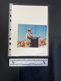 Colour photograph of an older woman in military uniform speaking at a podium.