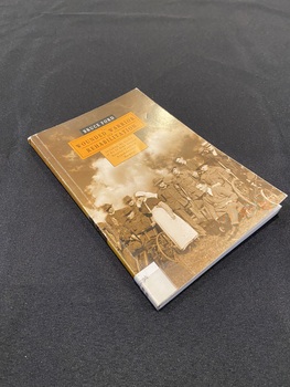 Small paperback with an orange spine with title printed down it and a white spine label taped to the bottom. The front cover shows a sepia toned image of a group of wounded soldiers on crutches and in wheelchairs with a nurse standing amongst them. There are two orange templates in the top centre of the page with the title information printed inside them in black print.