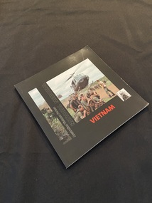 Square paperback book with a black cover. Red printed title on spine and cover. Front cover has a long thin photo image of jungle foliage down the left side, next to which is part of the title printed vertically down the page. On the right side is a photo of soldiers in a field with two helicopters taking off beside them and the word Vietnam printed in red text beneath.