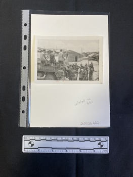 Small black and white photograph depicting a group of men in uniforms on and at the back of a truck