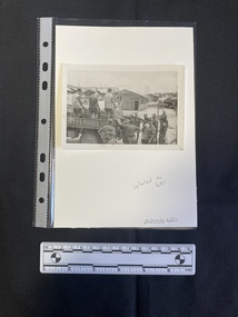 Small black and white photograph depicting a group of men in uniforms on and at the back of a truck