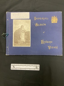 Blue album with a blue thread tied through the left edge. Gold writing on the cover and a black and white photograph of a stone memorial surrounded by people with heads bowed. There is a white sticker label in the top left corner with WWI handwritten.