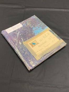 Spiral bound photograph album, cover is covered in an image of the Australian outback bush. There is a white sticker label in the top left and a label taped on with masking tape in the bottom right.
