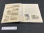 Inside layout shows seven black and white 2.7x3.7 photographs under protective plastic sheet on the left. The right side has a typed document with two photographs placed at the bottom, also under the protective plastic. The protective pages are held down by tape.