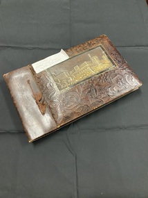 Ornate brown photograph album bound with thick brown thread tied at the front. An image of  David's Tower, Jerusalem is embedded in the front cover surrounded by an ornate embossed floral pattern.