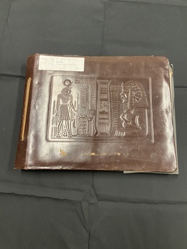 Brown leather cover bound with a tied leather strip down the left side. Embossed Egyptian image on the front cover. White sticker label in top left corner.