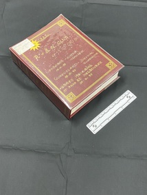 Burgundy photograph album with clear plastic cover. Spine displays multiple sets of three horizontal lines, the word 'photos' and four decorative symbols all printed in gold. Front cover has an ornate gold border, inside which is handwritten contents note. There is a white sticker label in the top left corner, partially covering a yellow star sticker that reads 'acid free pages'.