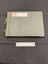 Green cloth bound photo album with two holes punched down the left side and tied with worn elastic. Large white sticker label towards the top that has WWII written on it in black ink.