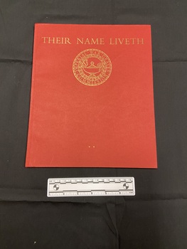 Red paperback book with thin spine. Front cover has the title printed across the top in gold, beneath is a circular emblem of the Imperial War Graves Commission.