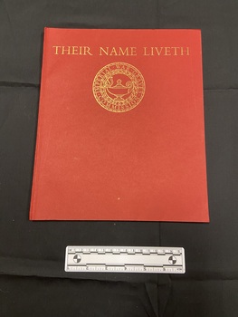 Red paperback book with thin spine. Front cover has the title printed across the top in gold, beneath is a circular emblem of the Imperial War Graves Commission.