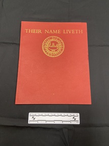 Red paperback book with thin spine. Front cover has the title printed across the top in gold, beneath is a circular emblem of the Imperial War Graves Commission.