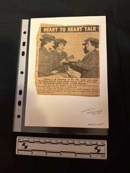 Newspaper clipping with a photograph of a woman holding a heart, talking to two young women.