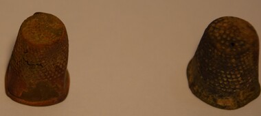 Two rusted and tarnished metal thimbles.