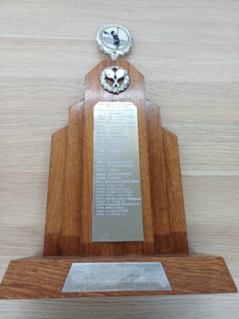Wooden trophy with golden disc at top and crossed tennis racquets below