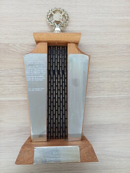 Two wooden pillars with black grille between, gold wreath and plates on pillars and base