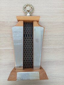 Two wooden pillars with black grille between, gold wreath and plates on pillars and base