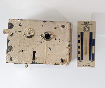 Door lock with the exterior portion painted cream. Some of the paint is flacking away. 