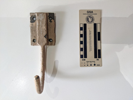 A hook with a wall mount that has some paint missing. The hook is facing the camera. 