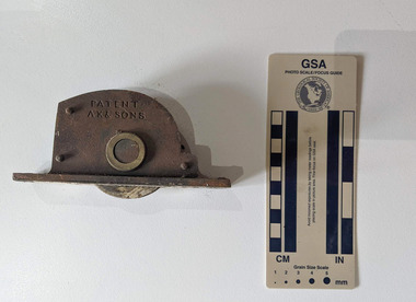 Corroded iron wall-mount with a circular pully mechanism. With Patent AK & Sons inscribed on the side 