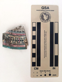 Brocken ceramic shard with a decorative design in pink, yellow and blue. 