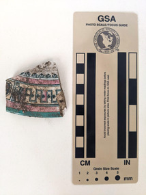 Brocken ceramic shard with a decorative design in pink, yellow and blue. 