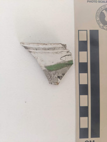 Ceramic shard with white gloss finish and black and green decorative pattern. 