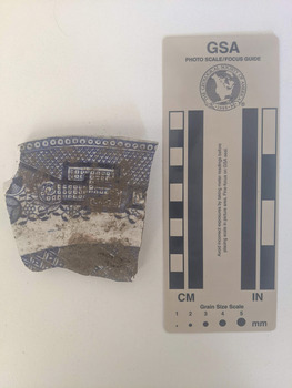 Ceramic shard with white glaze and blue decorative pattern. 