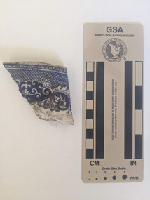 Ceramic shard with white glaze and blue decorative pattern. 