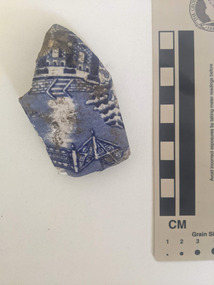 Ceramic shard with white glazed finish and a blue pictorial design.