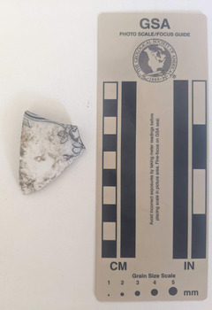 Ceramic shard with white glazed finish and a black floral design.