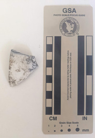 Ceramic shard with white glazed finish and a black floral design.