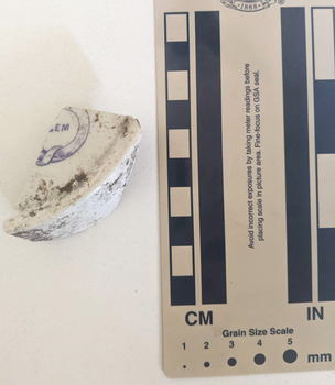 Ceramic shard with white glazed finish and a blue design with the letters E M