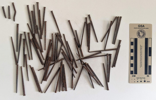 Collection of corroded nails with a rectangular head and square shaft that narrows to a blunt tip.