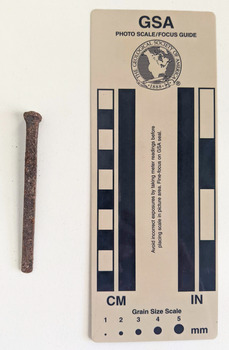 Corroded nail with a rectangular shaft that narrows to a blunt tip.