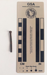 Corroded nail with rectangular shaft that narrows to a blunt tip.