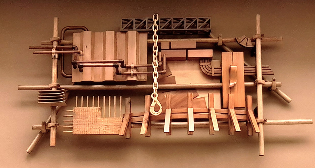 Wooden sculpture made to look like metal pipes and other fixings attached to a cream wall.
