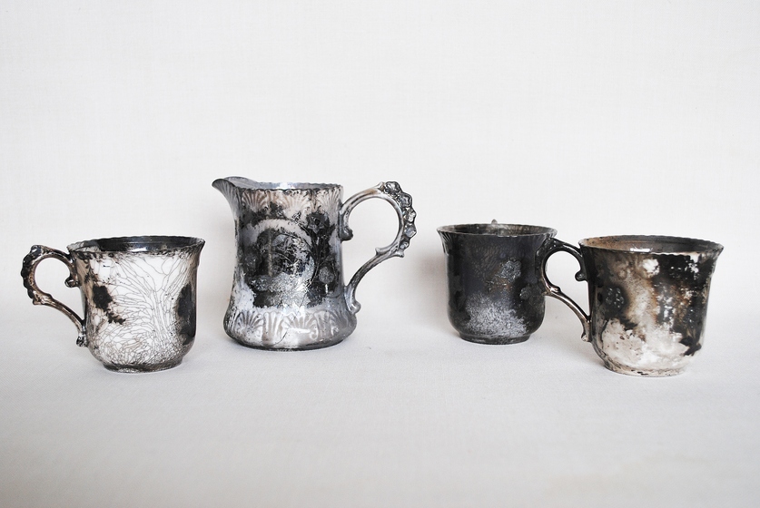 three blackened silver tea cups and jug