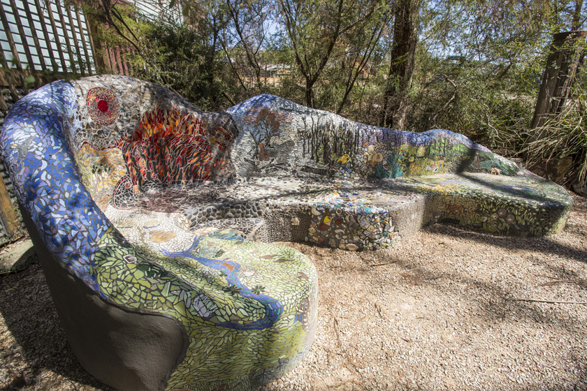 a large mosaic chair nestled in a park under trees