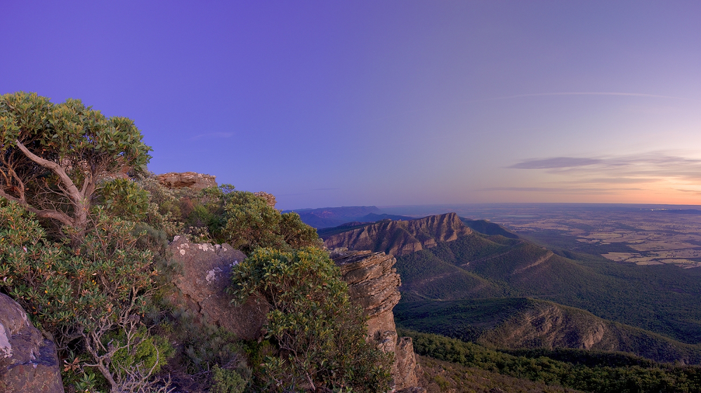 Breathtaking vista at dusk or dawn left foreground scrubby mountain top, right background distant mountains and sky