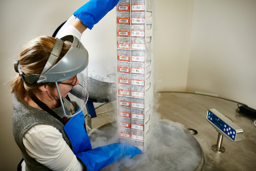 Woman wearing face shield, holding a tower of vials