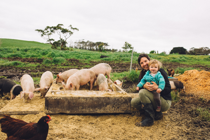 Woman holding her baby in front of pig pen