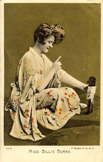 a woman sits cross-legged wearing a kimono and pointing at doll