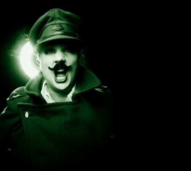 dark background with person with mustache and hat standing lit from behind