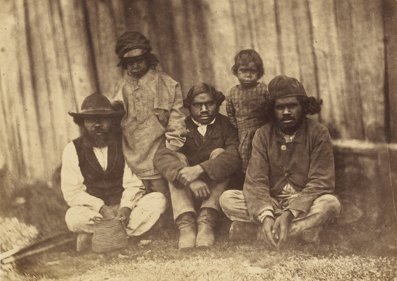 An early photograph, sepia with age, of three adult males sitting and two children standing at the base of a very large tree.
