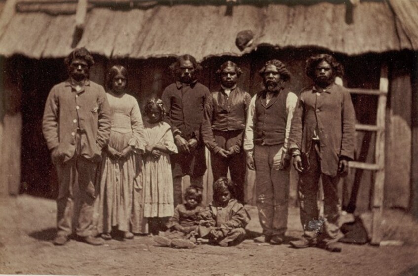 An early photograph, sepia with age, of a formally dressed family in front of a timber building.