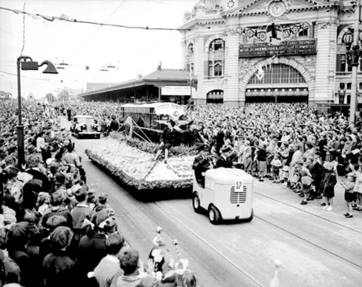 Floats parade past Flinders Street Station with a huge crowd of on-lookers