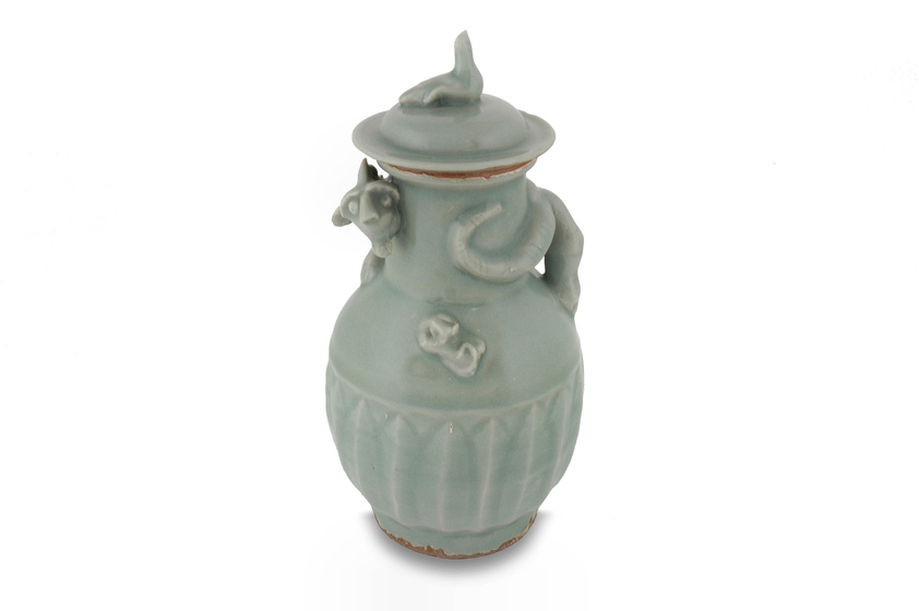a pale green-glazed ceramic funerary vase with a lid. A mythical creature curves its way around the top of the vase, offering protection.