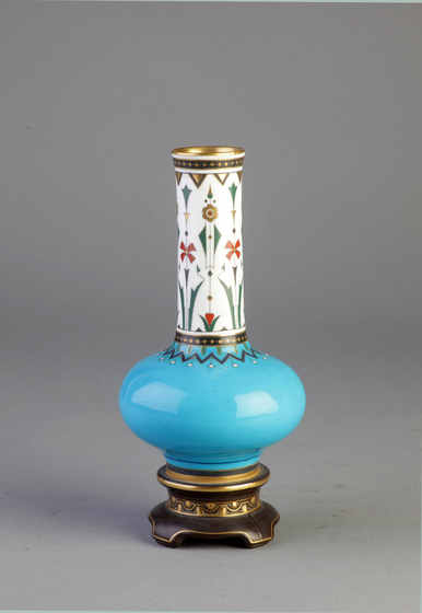 tall porcelain vase with enamelled cloisonne decoration. The neck of the vase is white with a stylised floral decoration, while the middle is turquoise and the foot features alternate gold and bronze decoration.