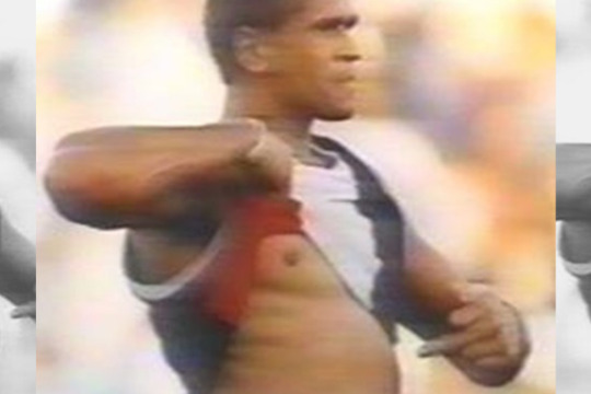 three repeated shots of an aboriginal football player raising his shirt and pointing to his skin